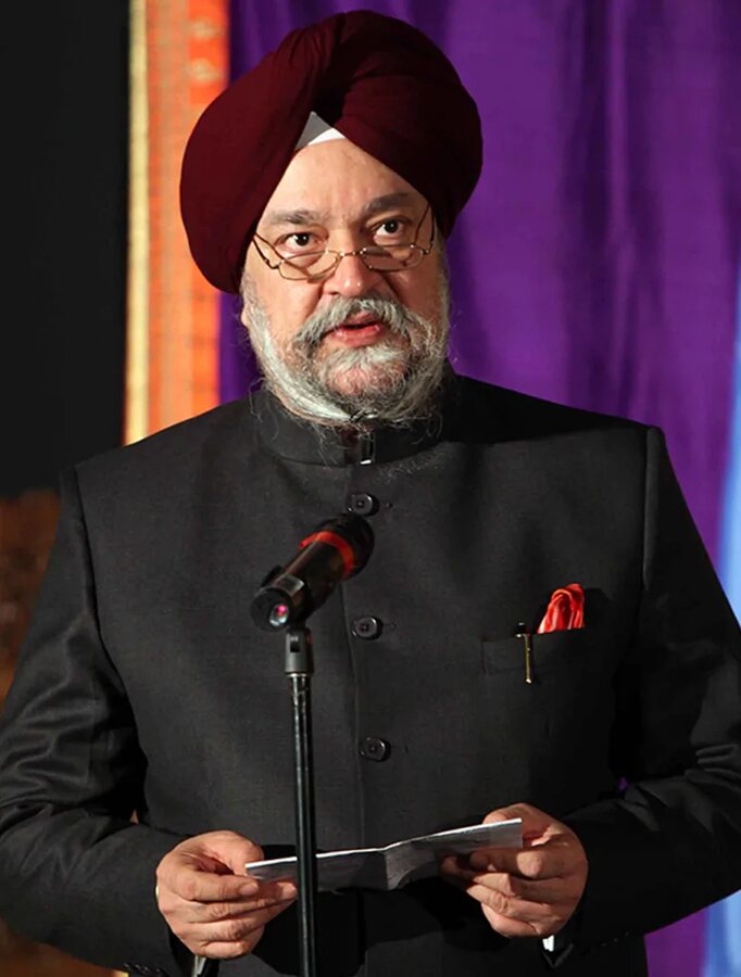 Hardeep Singh Puri in a black bandhgala suit reading remarks at a microphone in front of a purple curtain