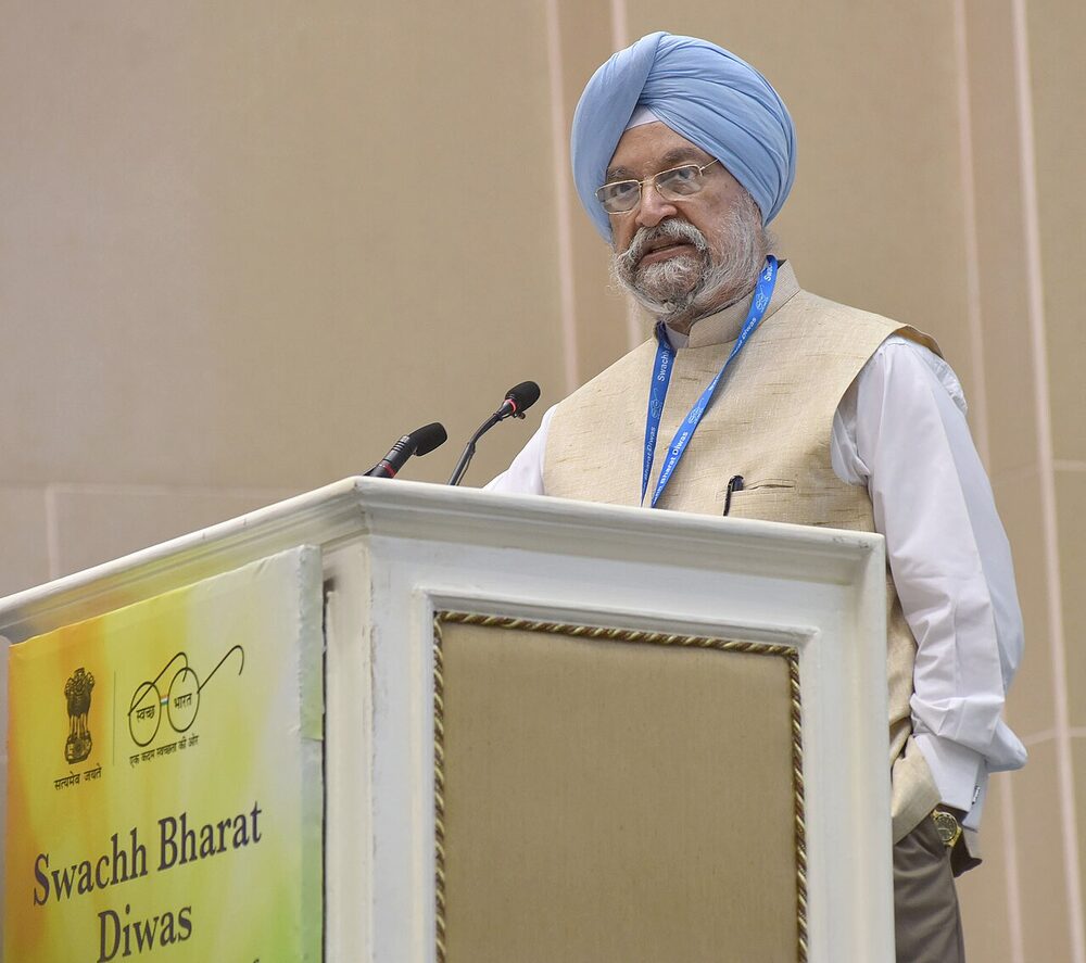 Hardeep Singh Puri in a light blue turban speaking at a podium marked Swachh Bharat Diwas