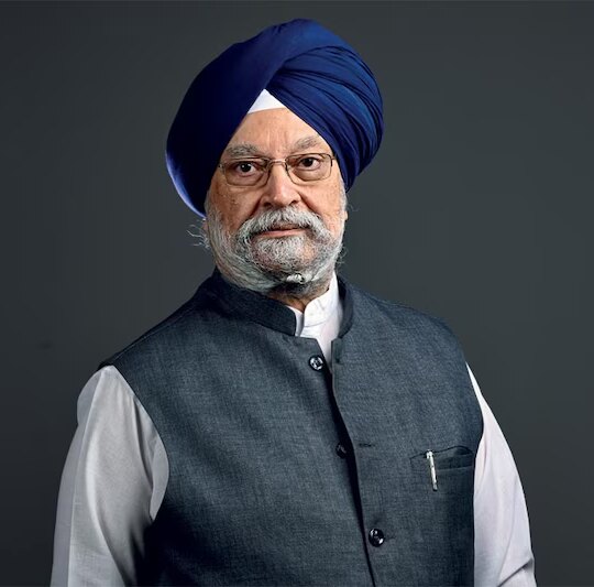 Portrait of Hardeep Singh Puri wearing a blue turban, white kurta and grey bandhgala waistcoat against a dark background